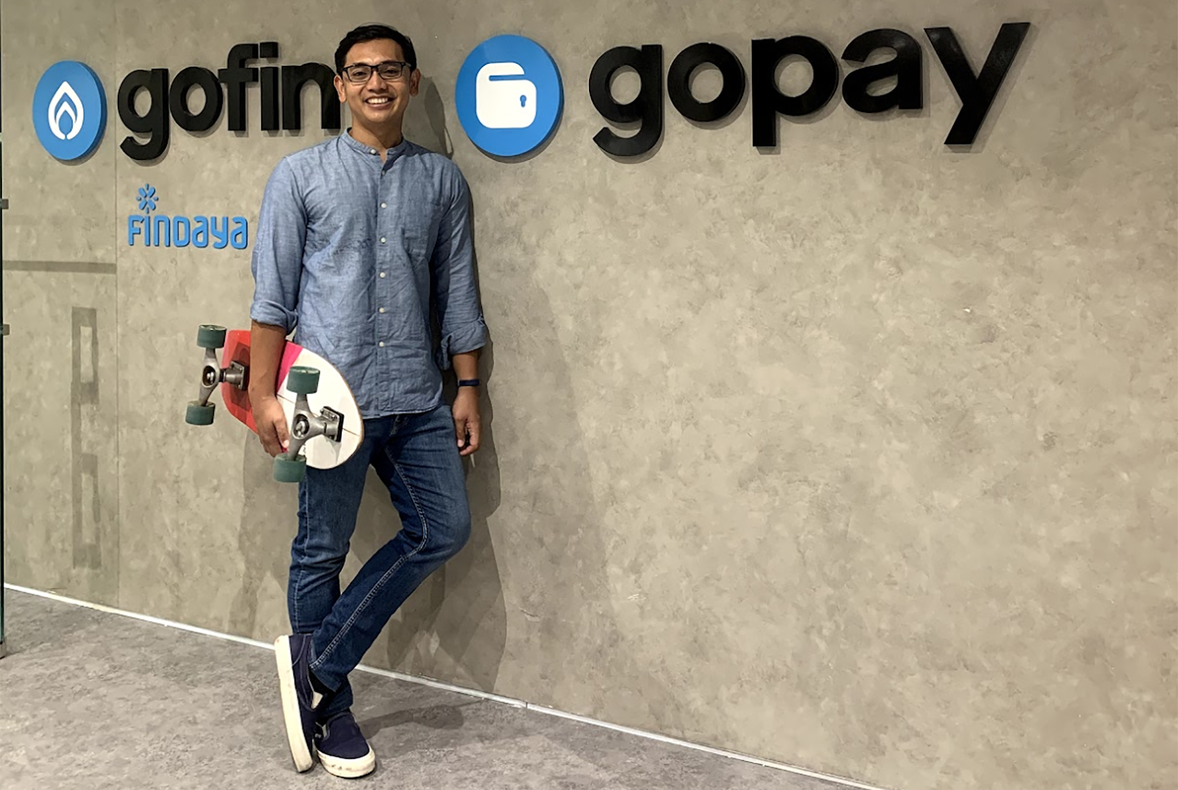 Aldi Haryopratomo standing in front of a GoPay sign holding a skateboard.